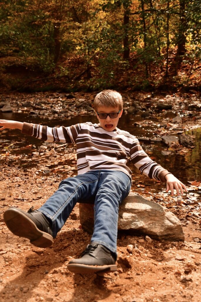 A young boy falling backwards off of a rock.